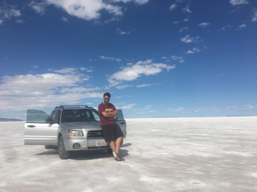 Man leaning against silver Subaru in the middle of a salt flat