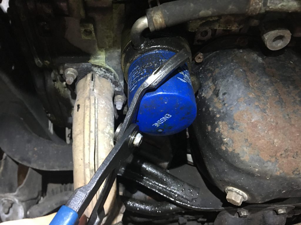 Using a pair of oil filter pliers to remove the oil filter.