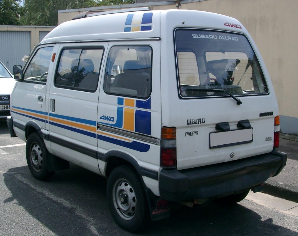 Rear of white Subaru microvan showing E12 and Subaru Allrad Decals