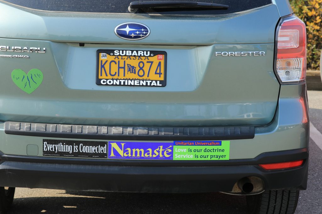 Green Subaru Forester with a variety of bumper stickers spelling out "Everything is connected" "Namaste" and "Unitarian Universalism: Love is our doctrine, Service is our prayer".