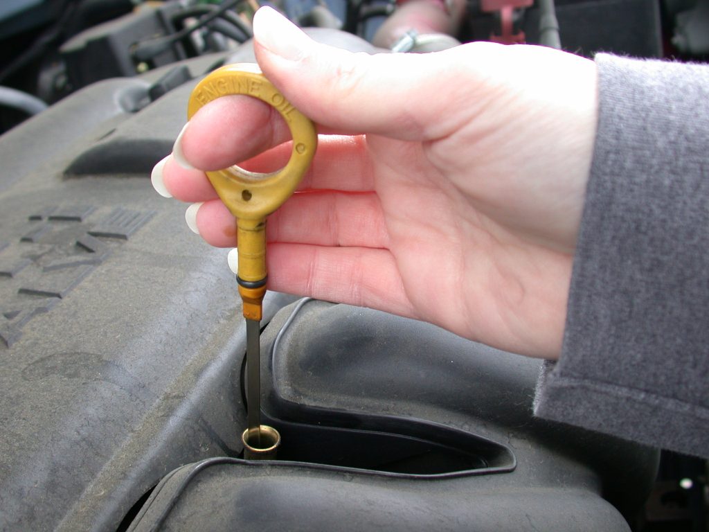 Woman's hand pulling dipstick from engine. 